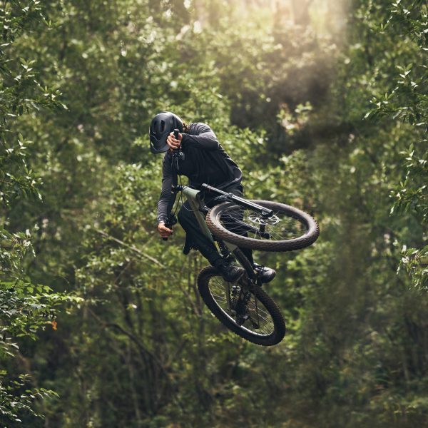 Cycling, bicycle jump and sports man travel in Japan nature forest for adventure and extreme sport journey. Trees, stunt and mountain bike rider or cyclist training in woods for exercise and fitness.